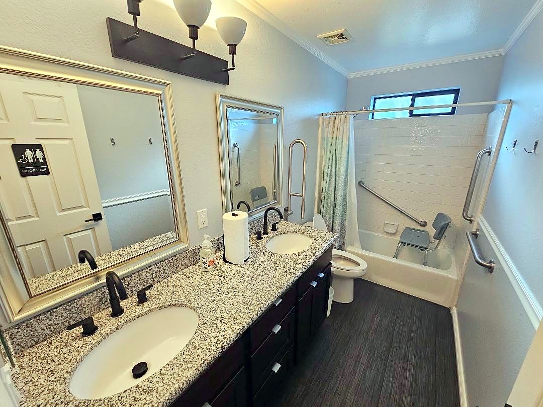 Bathroom with double vanity, grab bars, and a curtained tub-shower