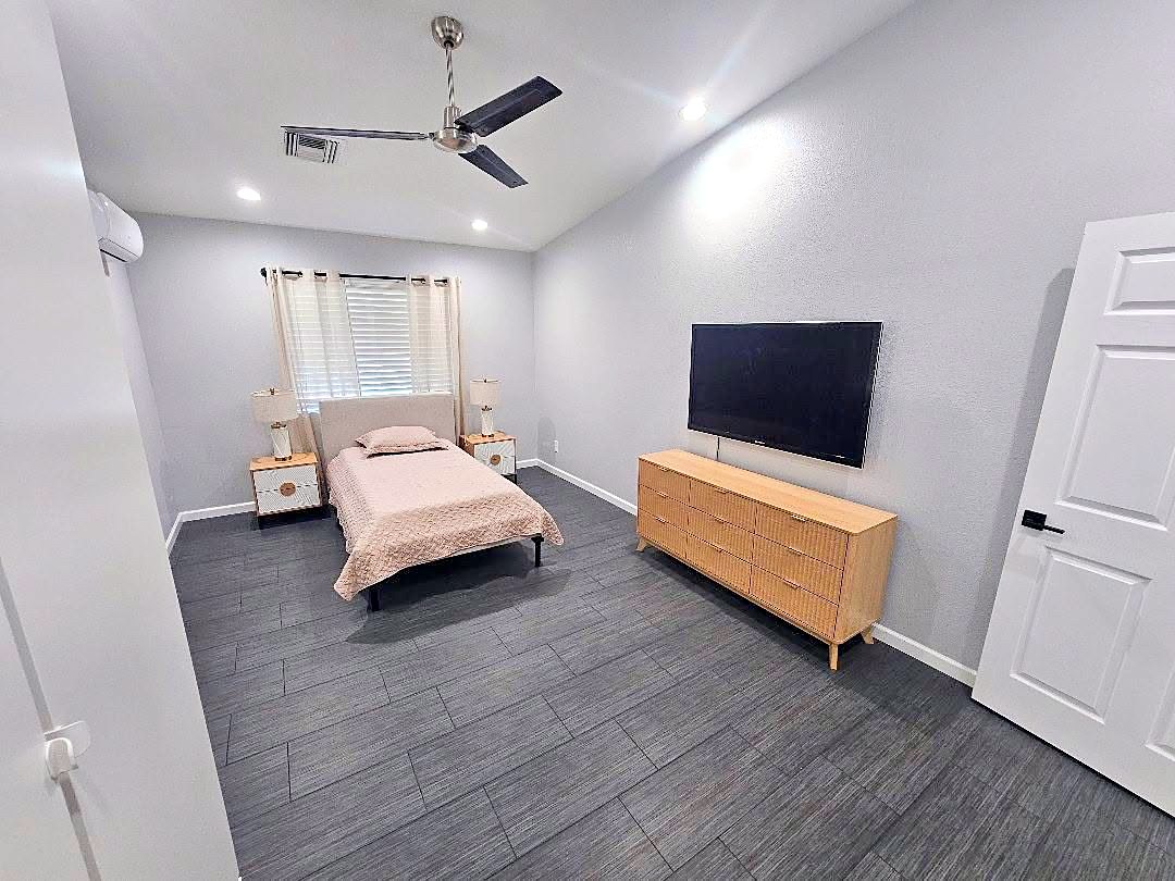 Private bedroom with a single bed, dresser, television, and window